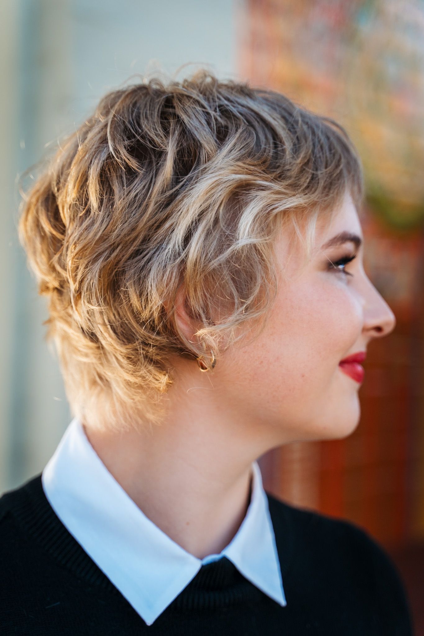 Woman with short, wavy blonde hair, wearing a black sweater with a white collared shirt, looking to the right.