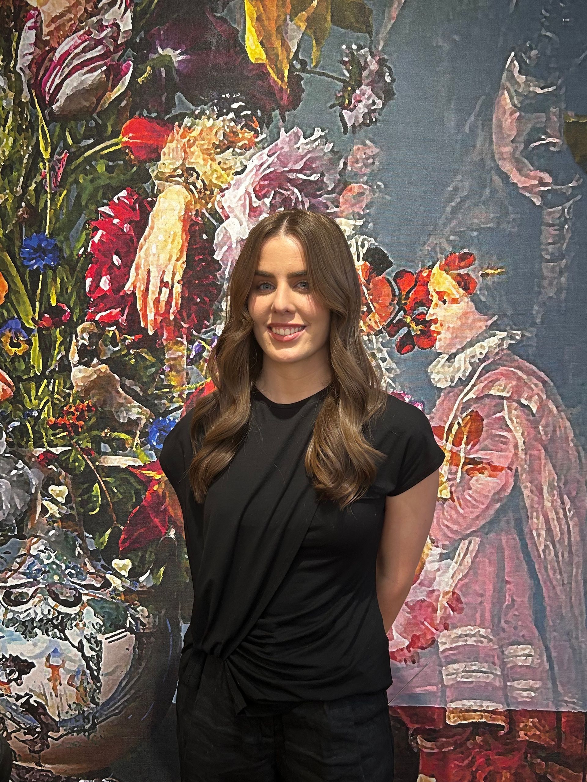 Smiling woman in a black top standing before a colorful mural