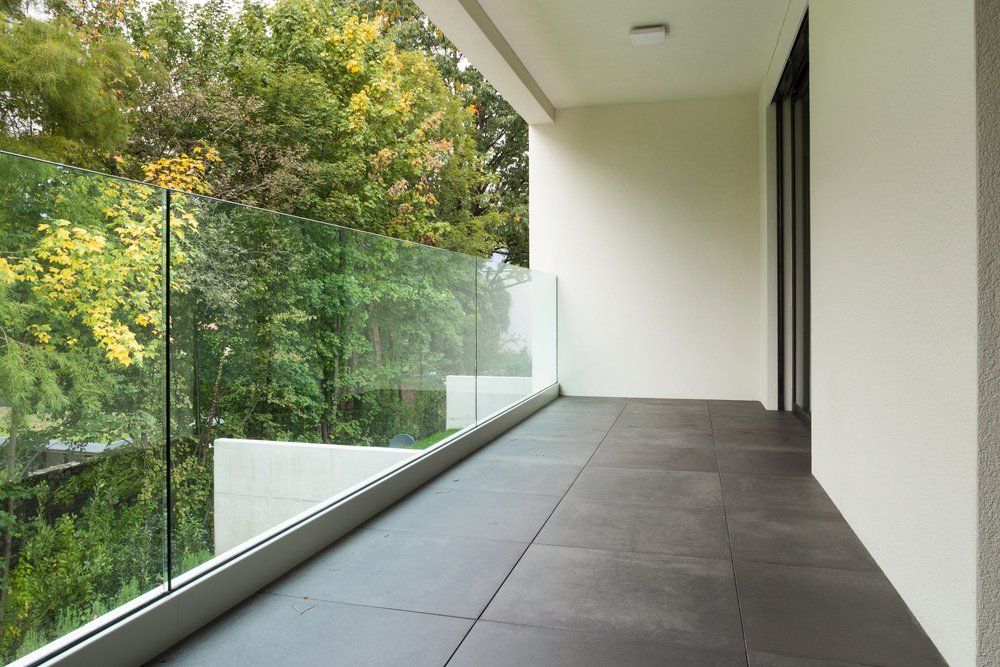 An empty balcony with a glass railing and trees in the background