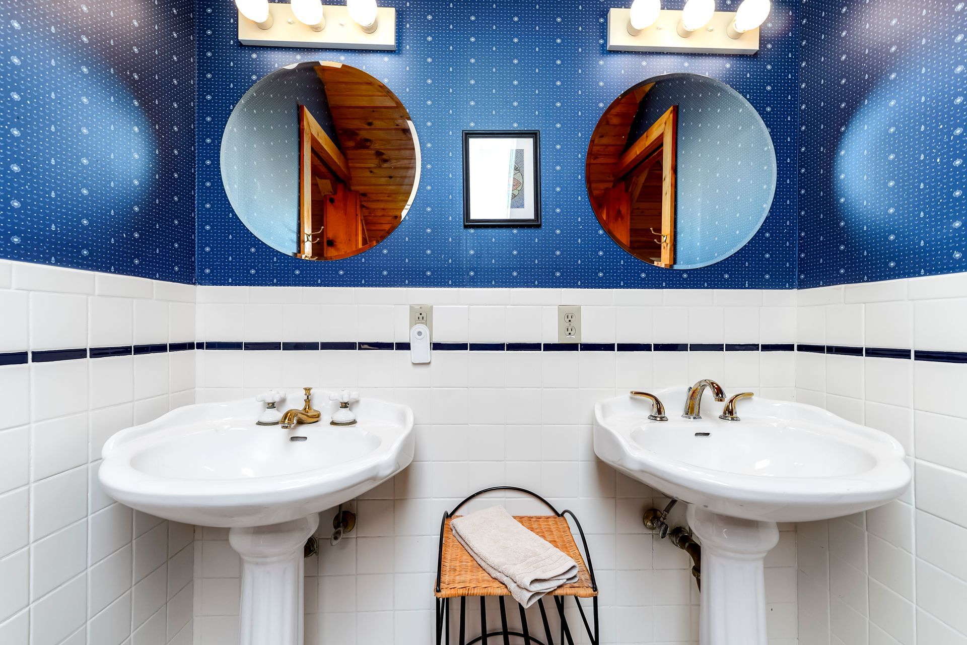 Public restroom with two white sinks, round mirrors, blue speckled walls, and a hand towel basket between them