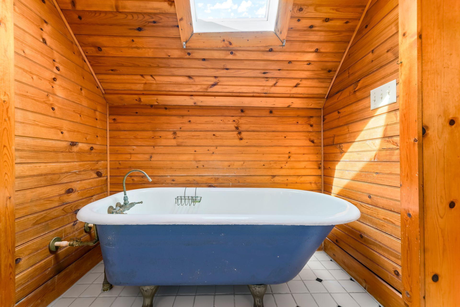 Blue freestanding bathtub in a wood-paneled bathroom with a skylight and tiled floor