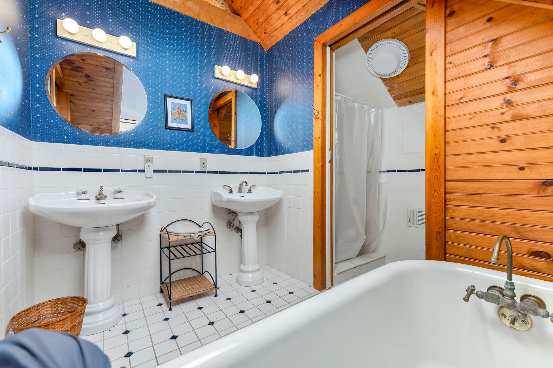 Blue and wood-paneled bathroom with twin sinks, tub, and shower stall