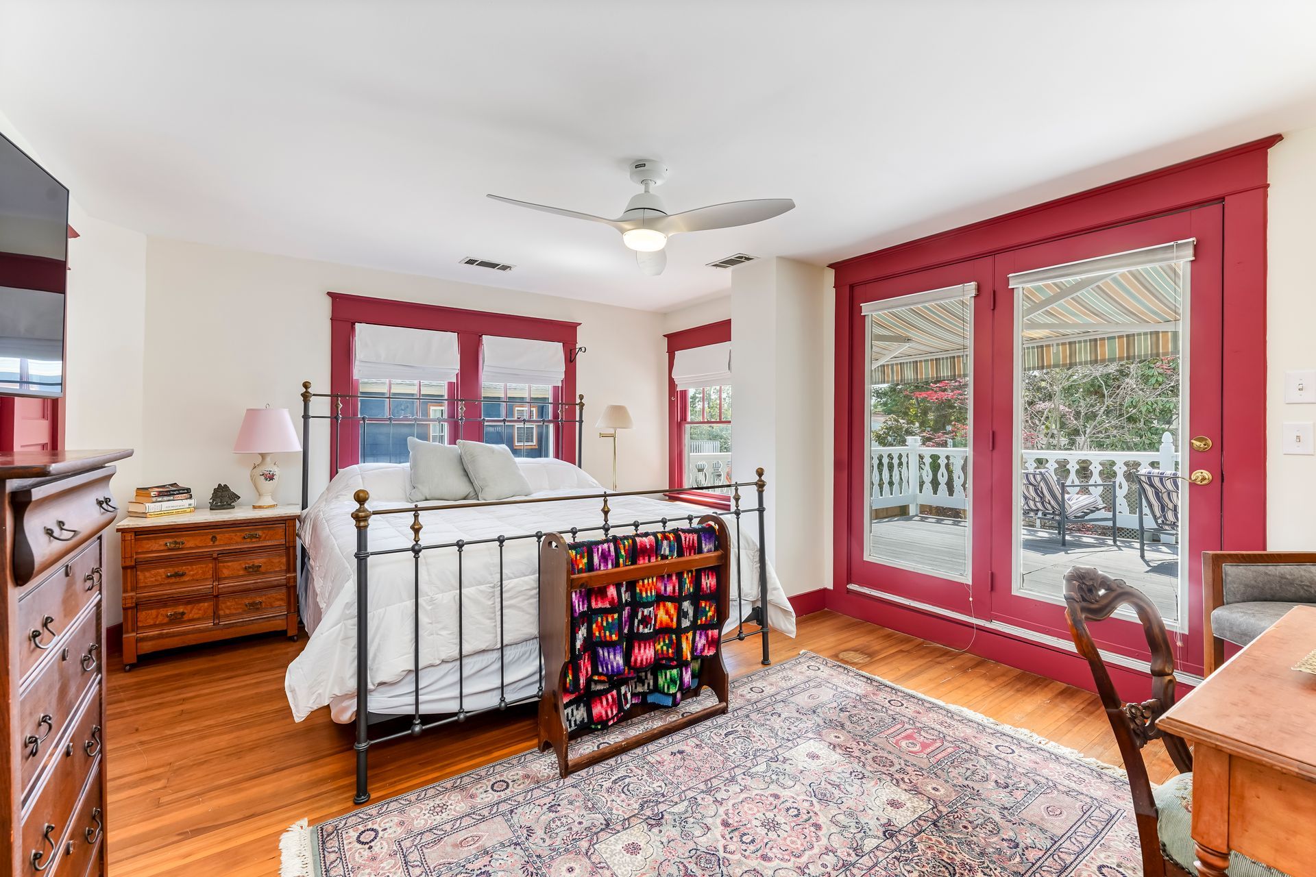 Bright bedroom with white bed, red-trimmed windows, hardwood floor, and patterned rug
