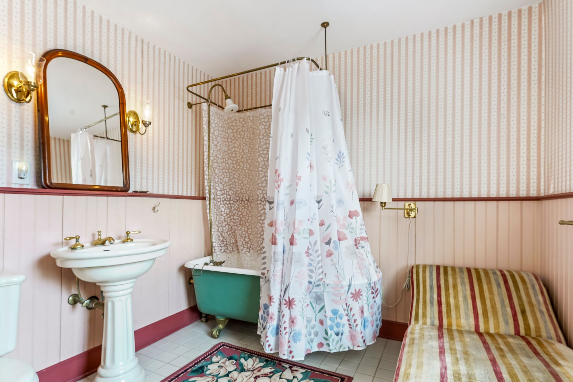 Vintage bathroom with striped wallpaper, pedestal sink, clawfoot tub, shower curtain, and striped sofa seat