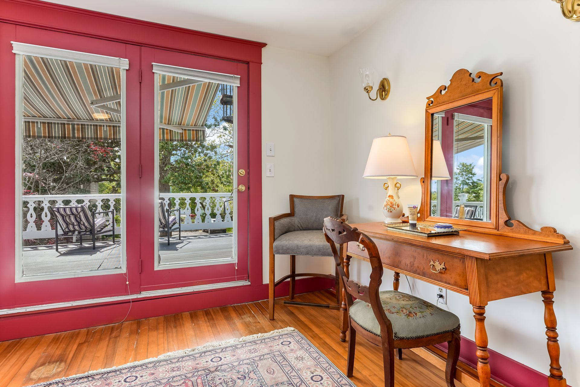 Bright pink-framed patio doors beside a wooden desk, chair, lamp, and wall mirror in a sunlit room