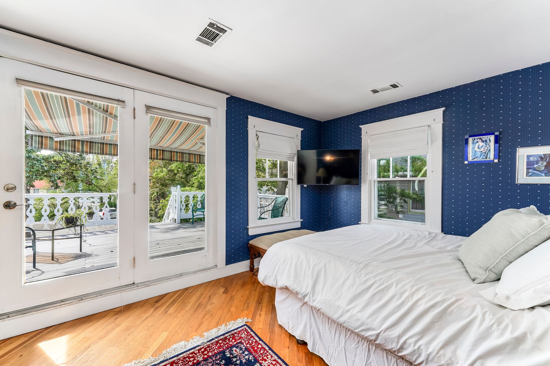 Bright bedroom with blue wallpaper, white bed, large windows, and hardwood floors.