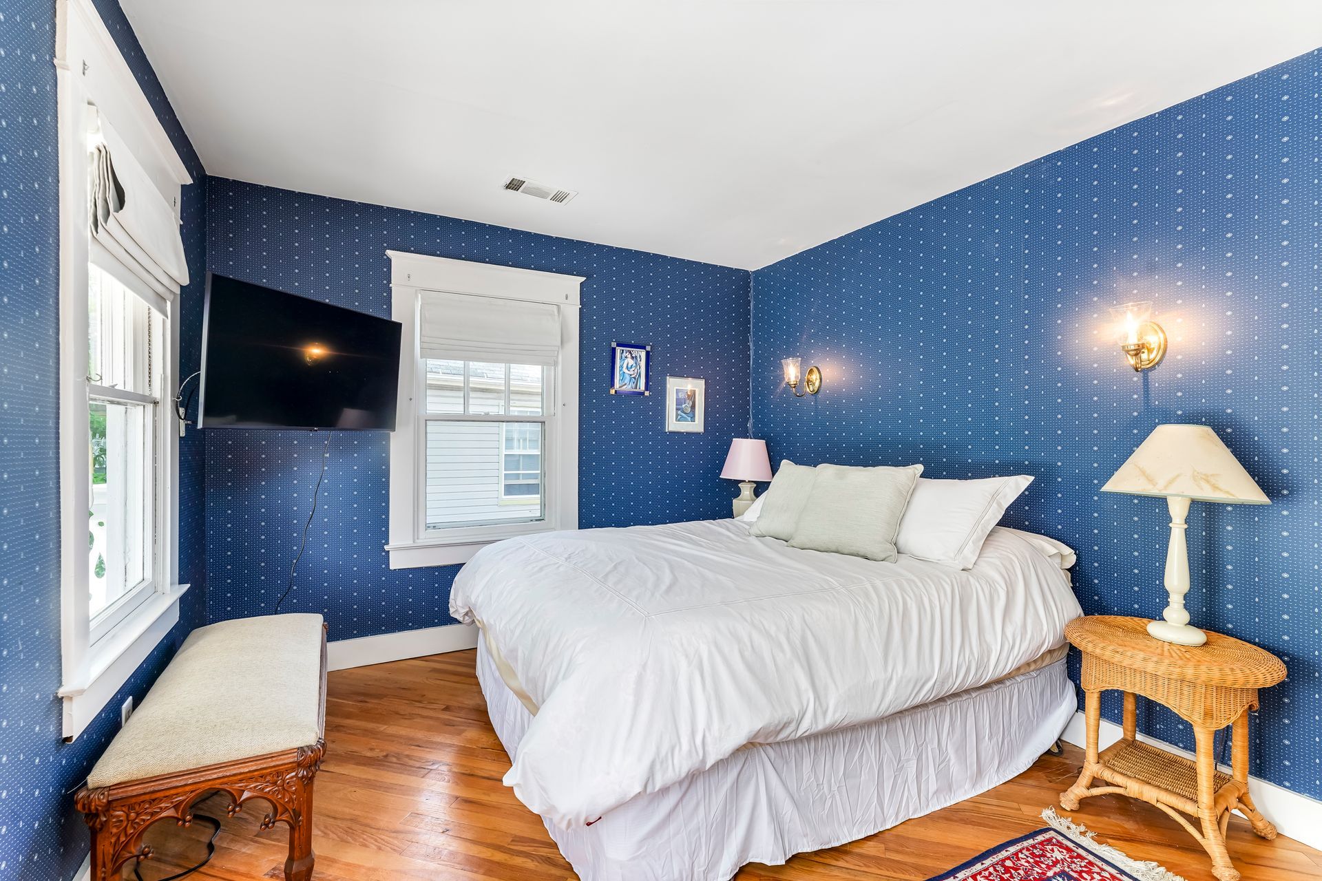 Blue bedroom with a white bed, wall-mounted TV, window seats, and wooden nightstands