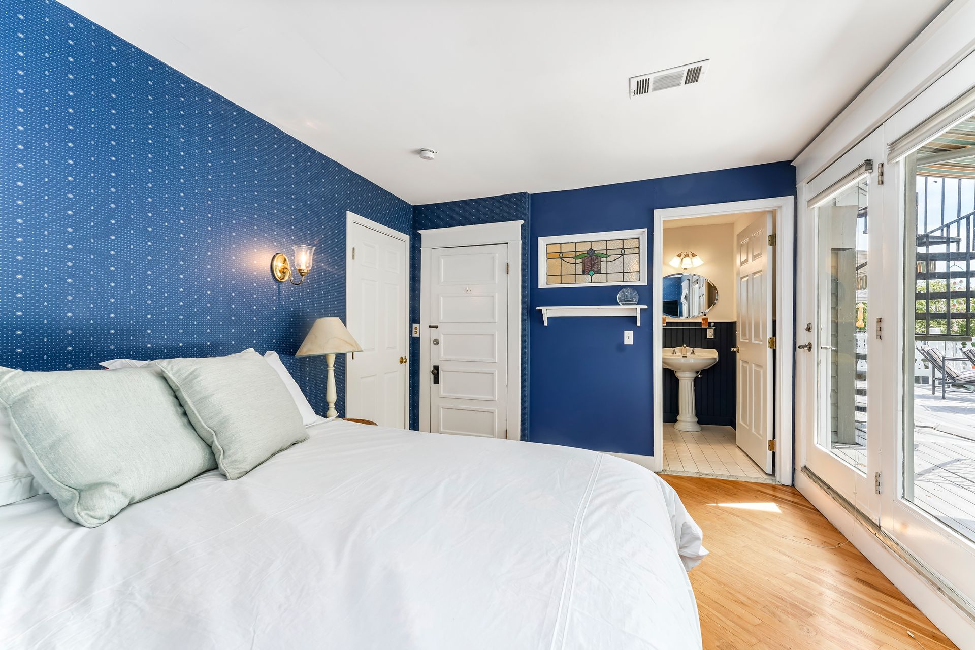 Bright bedroom with blue accent wall, white bed, and glass doors leading to a bathroom.