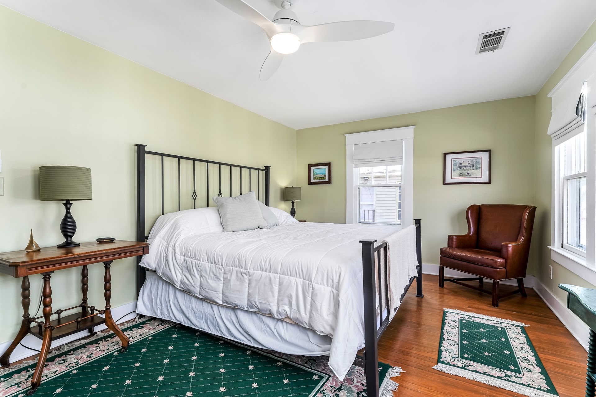 Bright bedroom with white bed, green rug, leather chair, and wooden side tables.