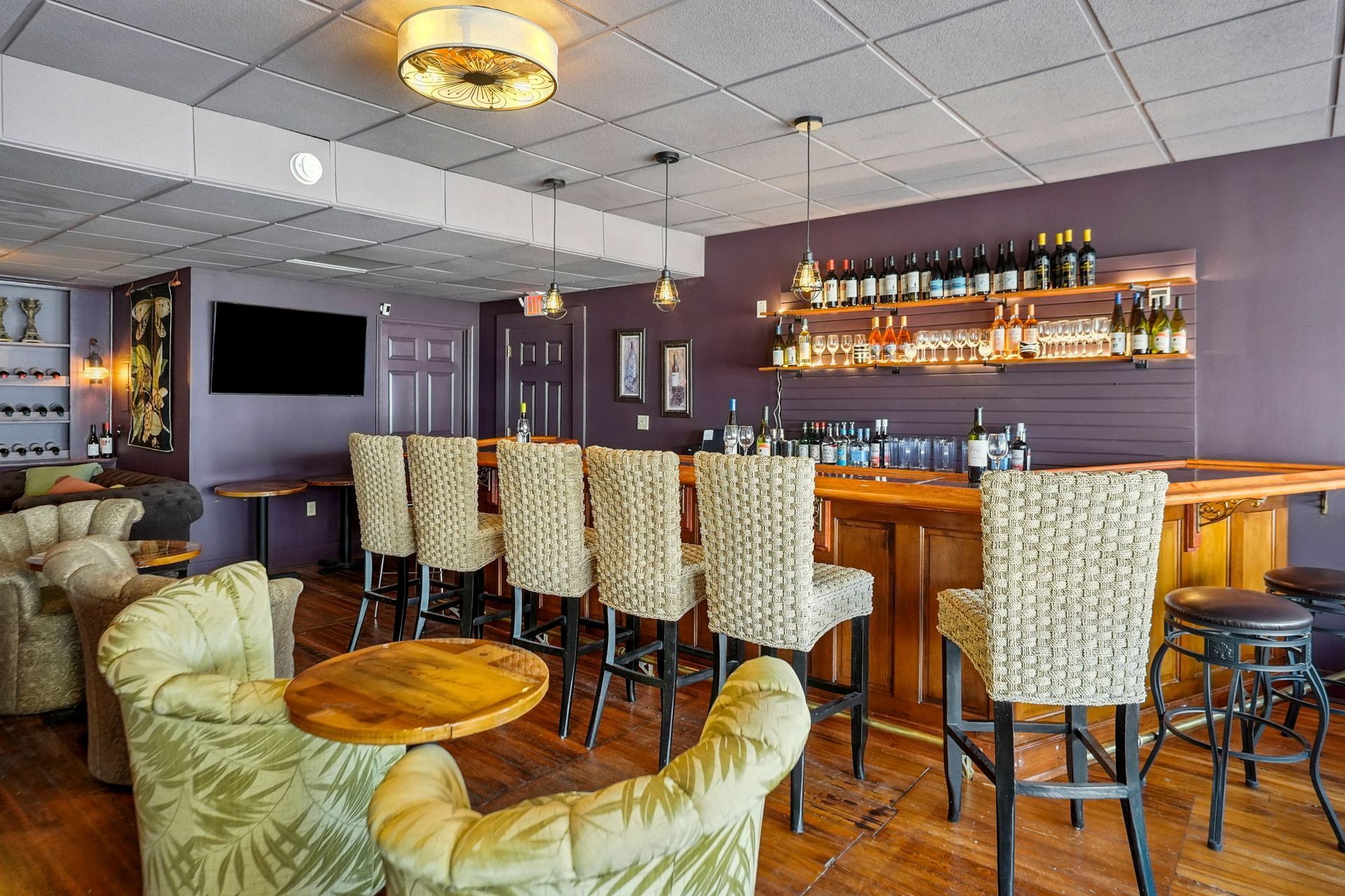 Modern lounge bar with high stools, leather chairs, shelves of bottles, and a wall-mounted TV