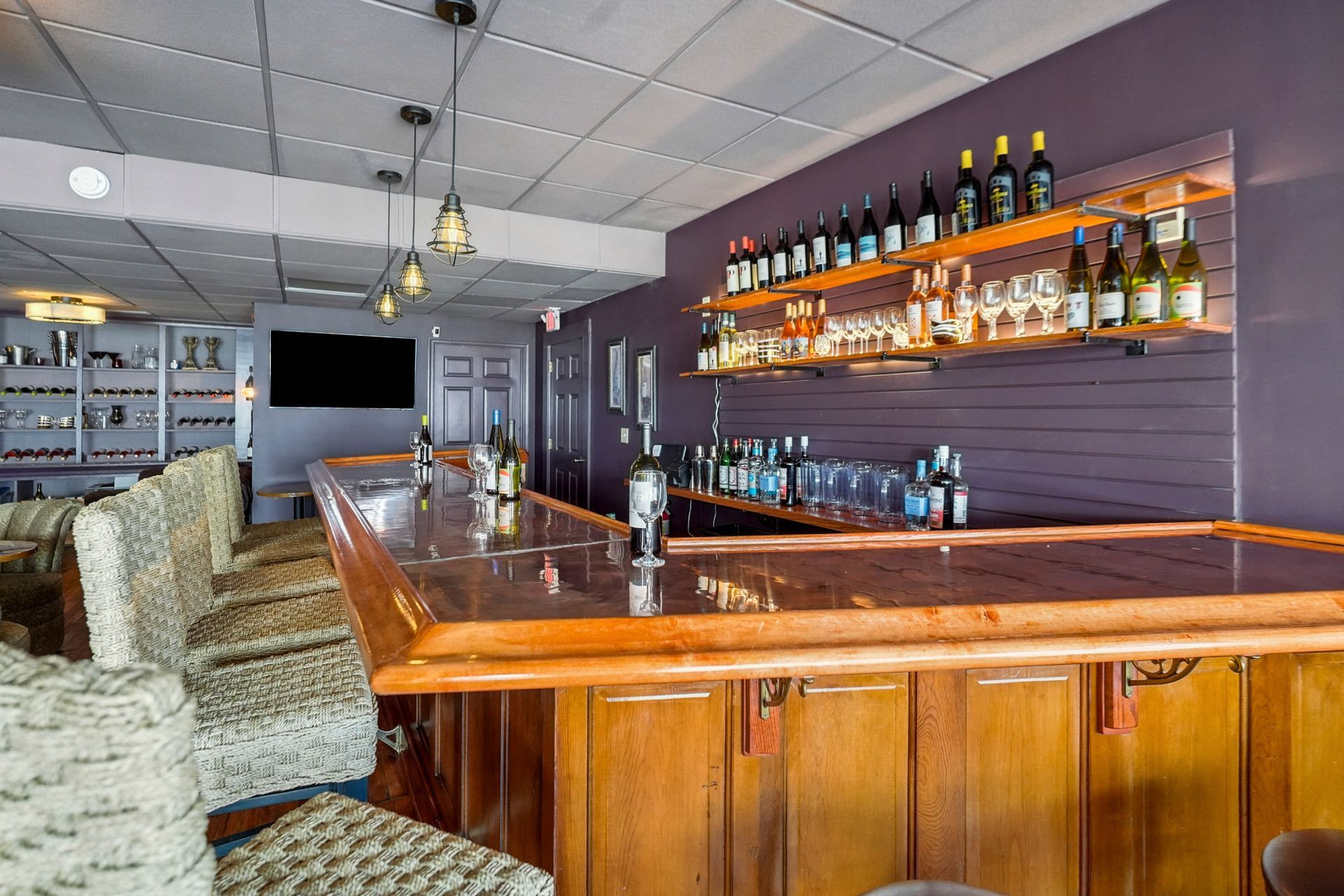 Empty bar interior with wooden counter, stools, and liquor bottles on shelves