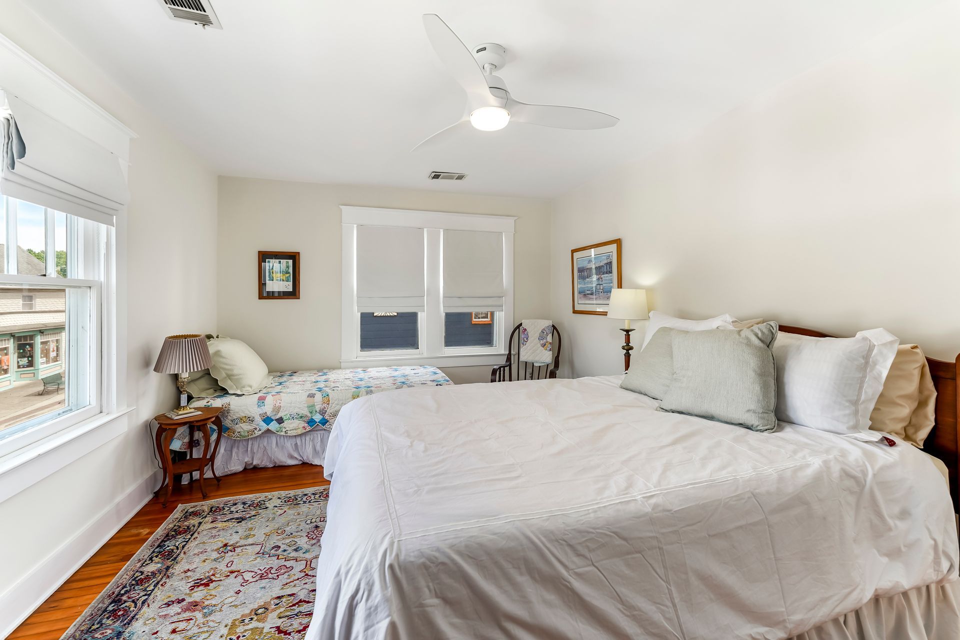 Bright bedroom with white bed, hardwood floors, and windows letting in daylight