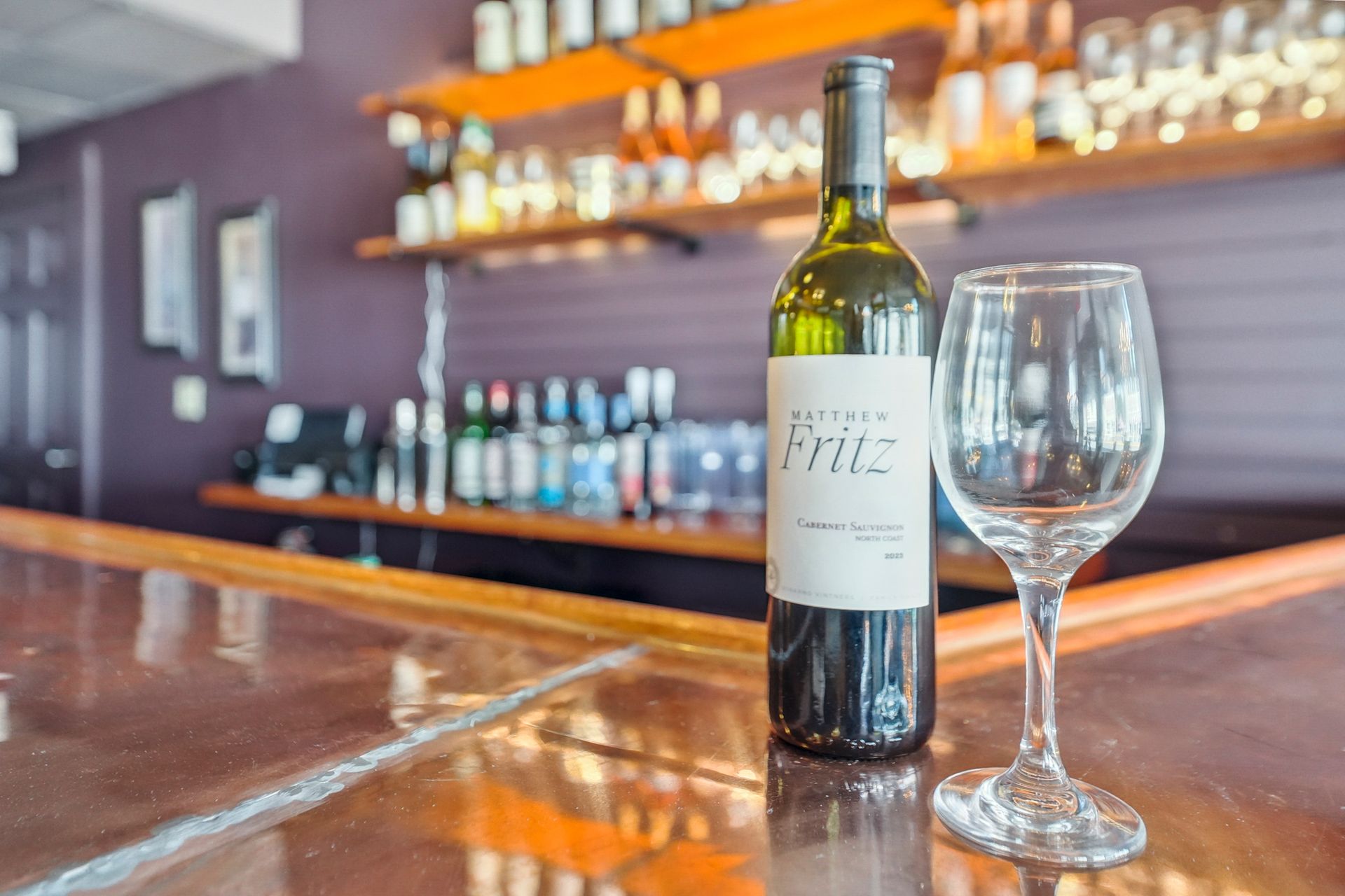 Wine bottle and empty glass on a polished bar counter with blurred bottles in the background