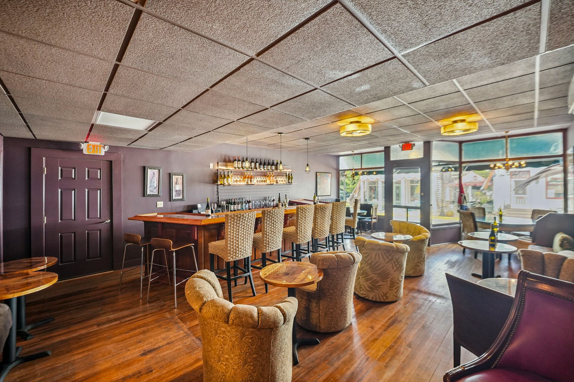 Cozy lounge bar with wooden floors, stools, round chairs, and large windows overlooking a patio