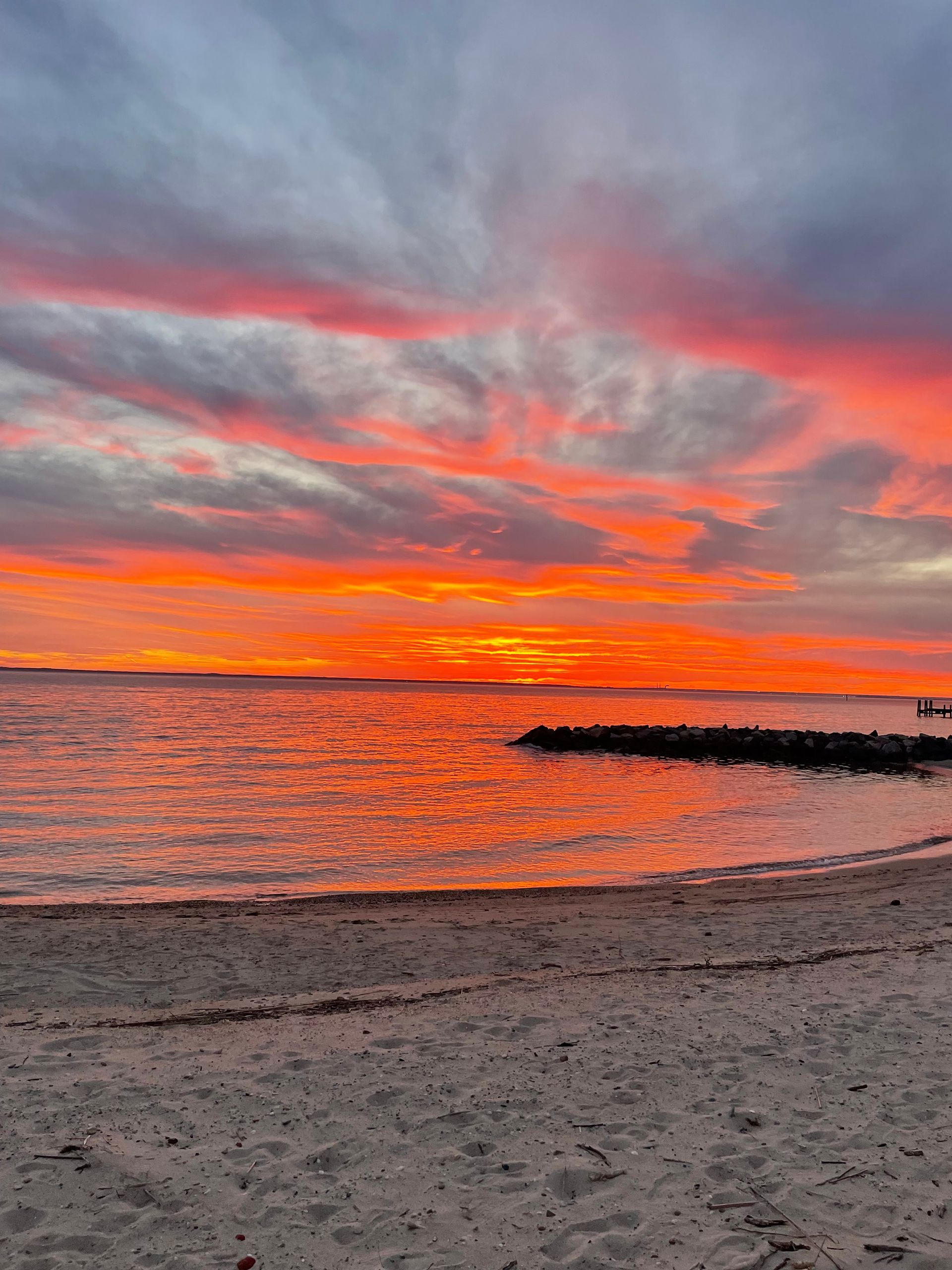 Sunset over a beach with orange clouds above a wooden fence and sand dunes