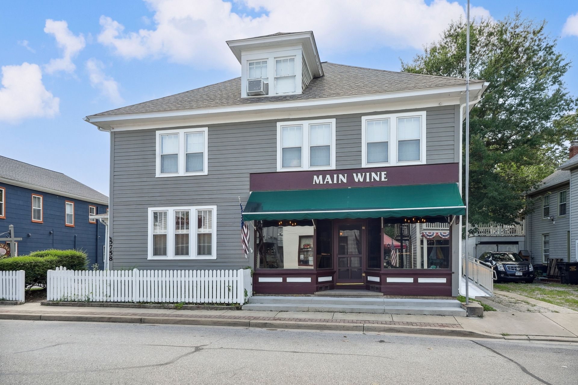 Gray storefront with a green awning reading “MAIN WINE” on a residential street