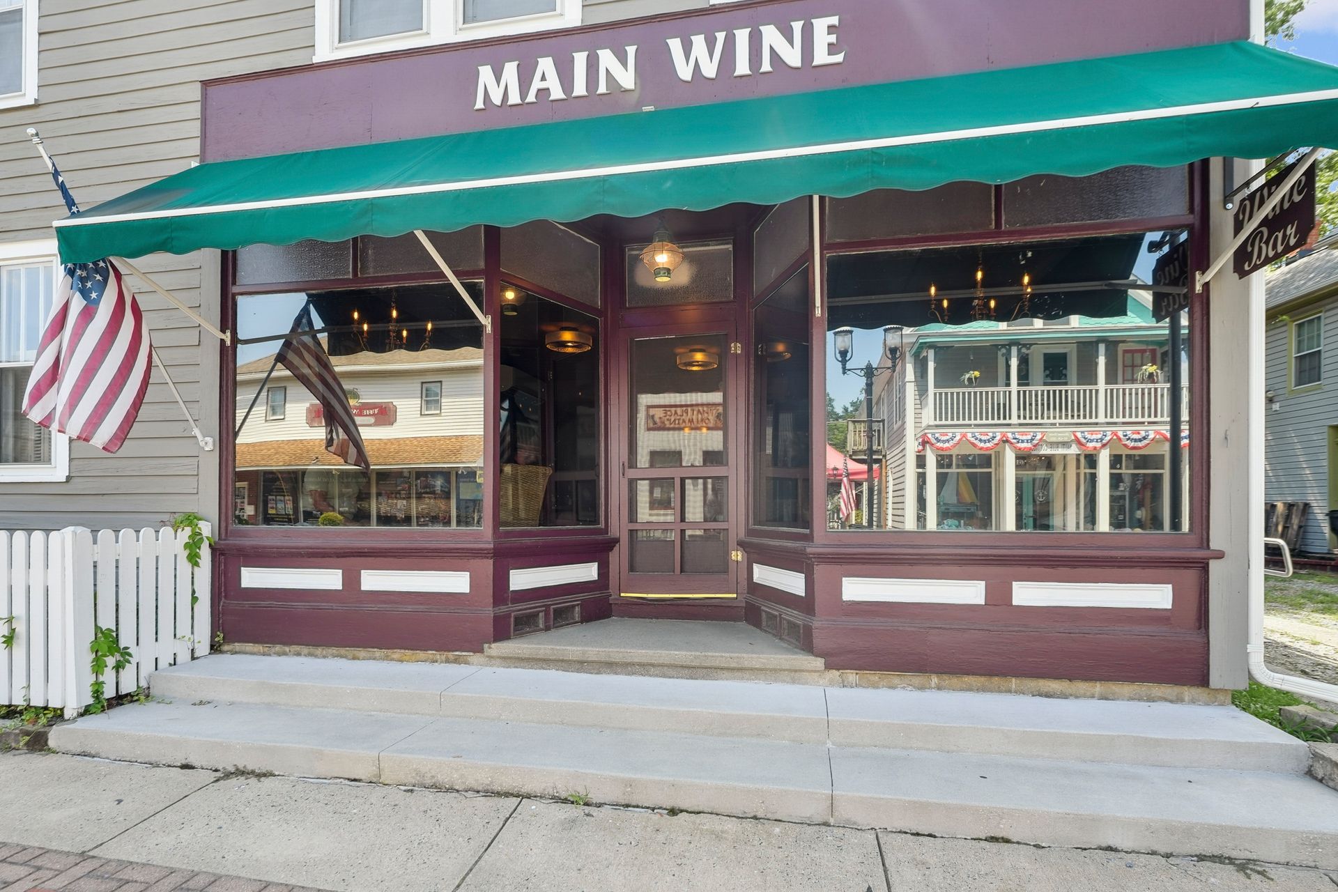 Storefront with teal awning and “MAIN WINE” sign, with American flag and large display windows.