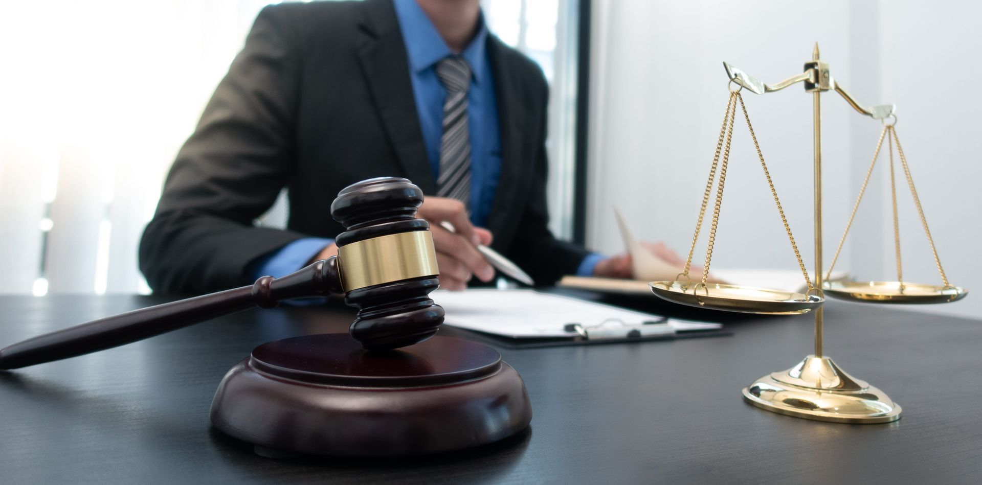 Gavel on desk with lawyer in suit and brass scales of justice in the background