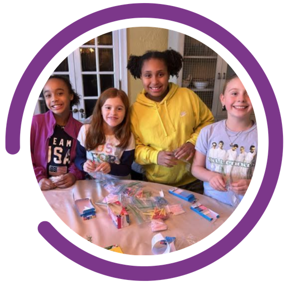 Kindness Grows Here - young girls making crafts around a kitchen table. Purple semicircle graphic outside of the image 