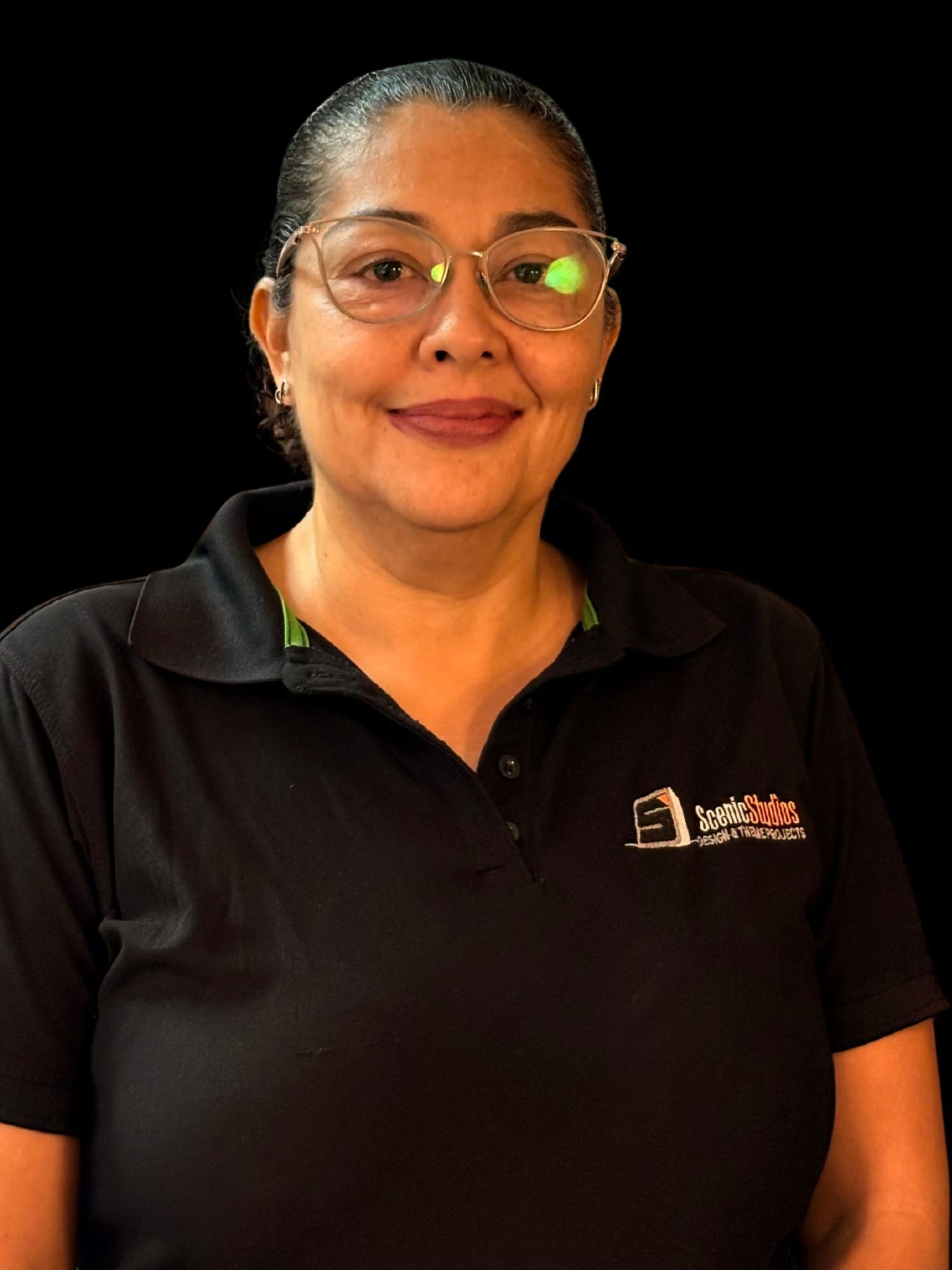 Retrato de una mujer sonriente con gafas y una camisa polo negra, sobre un fondo negro