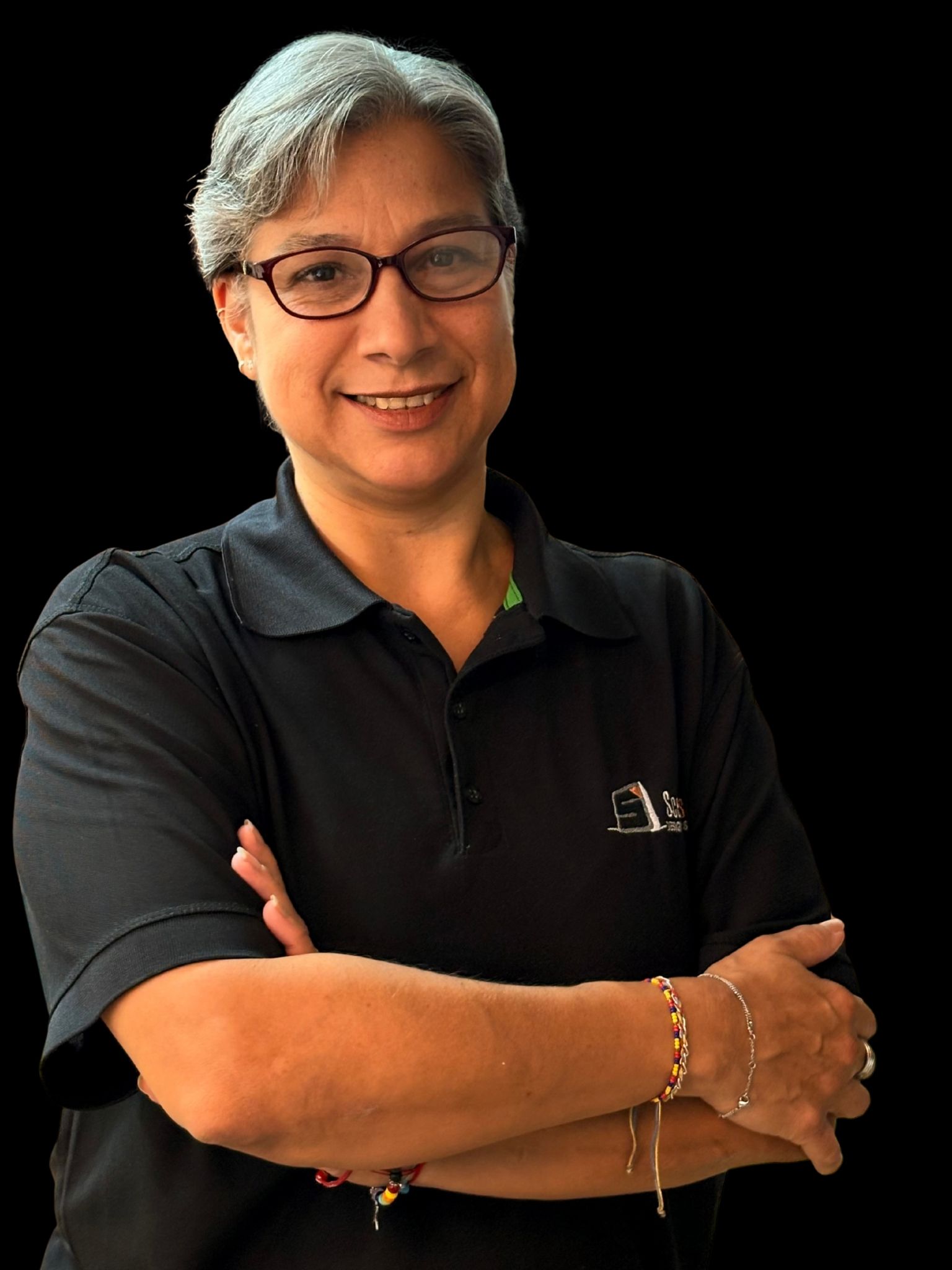Persona sonriente, de pelo corto y canoso y con gafas, que lleva un polo negro y tiene los brazos cruzados sobre un fondo negro