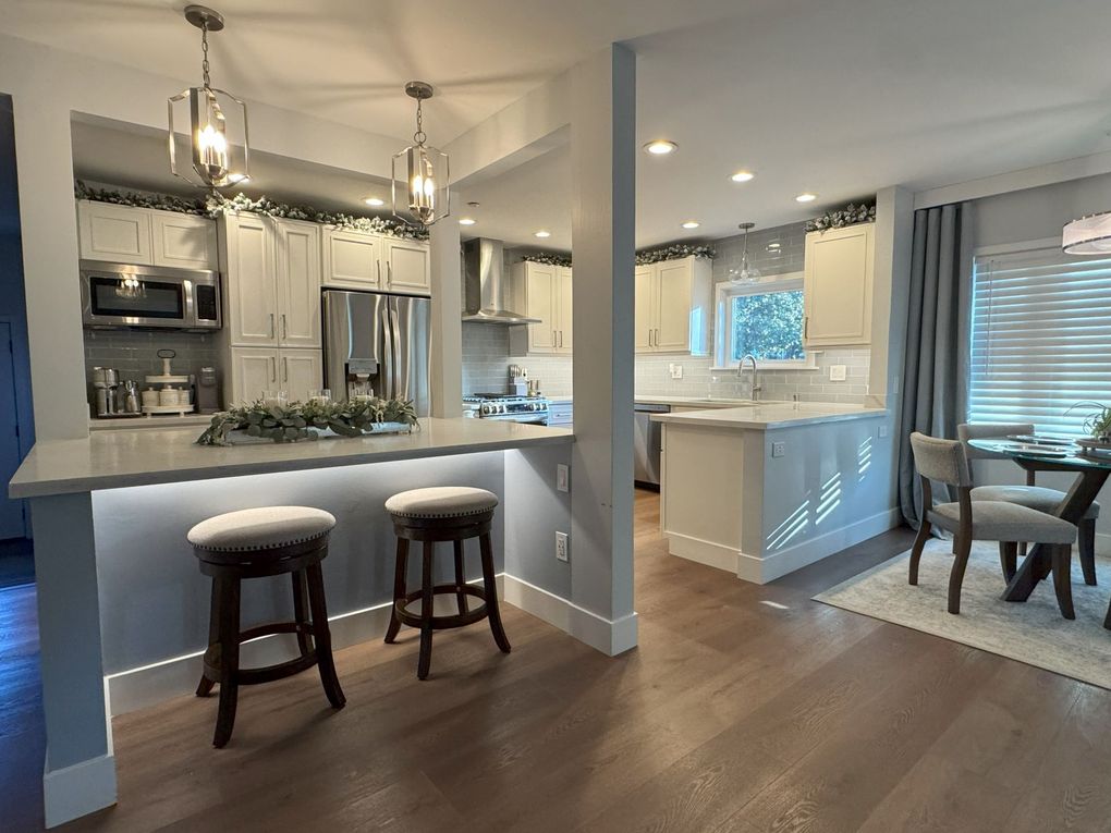 Modern kitchen with light gray cabinets, stainless steel appliances, and a breakfast bar with stools.
