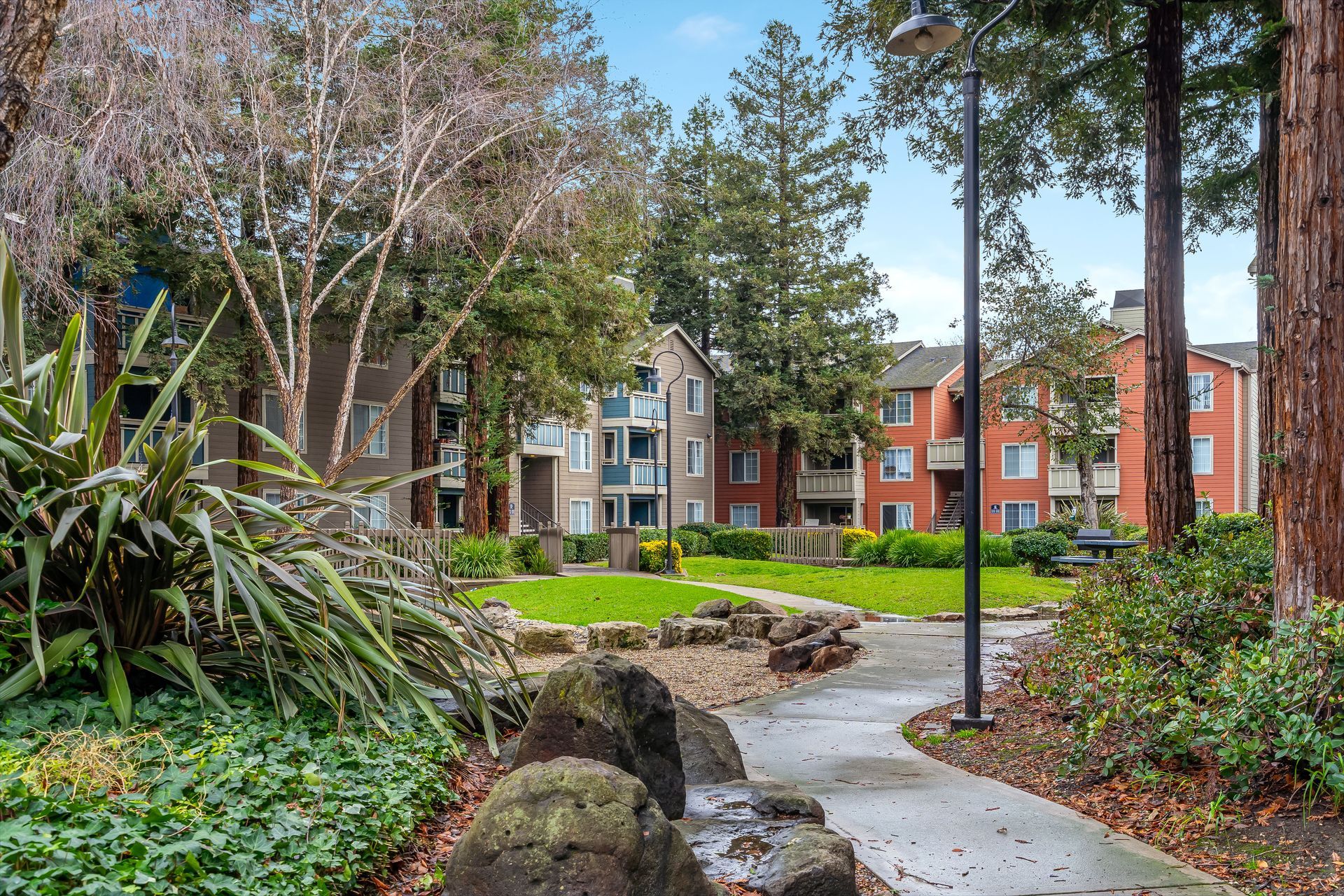 Apartment complex with a walking path, trees, and green grass.