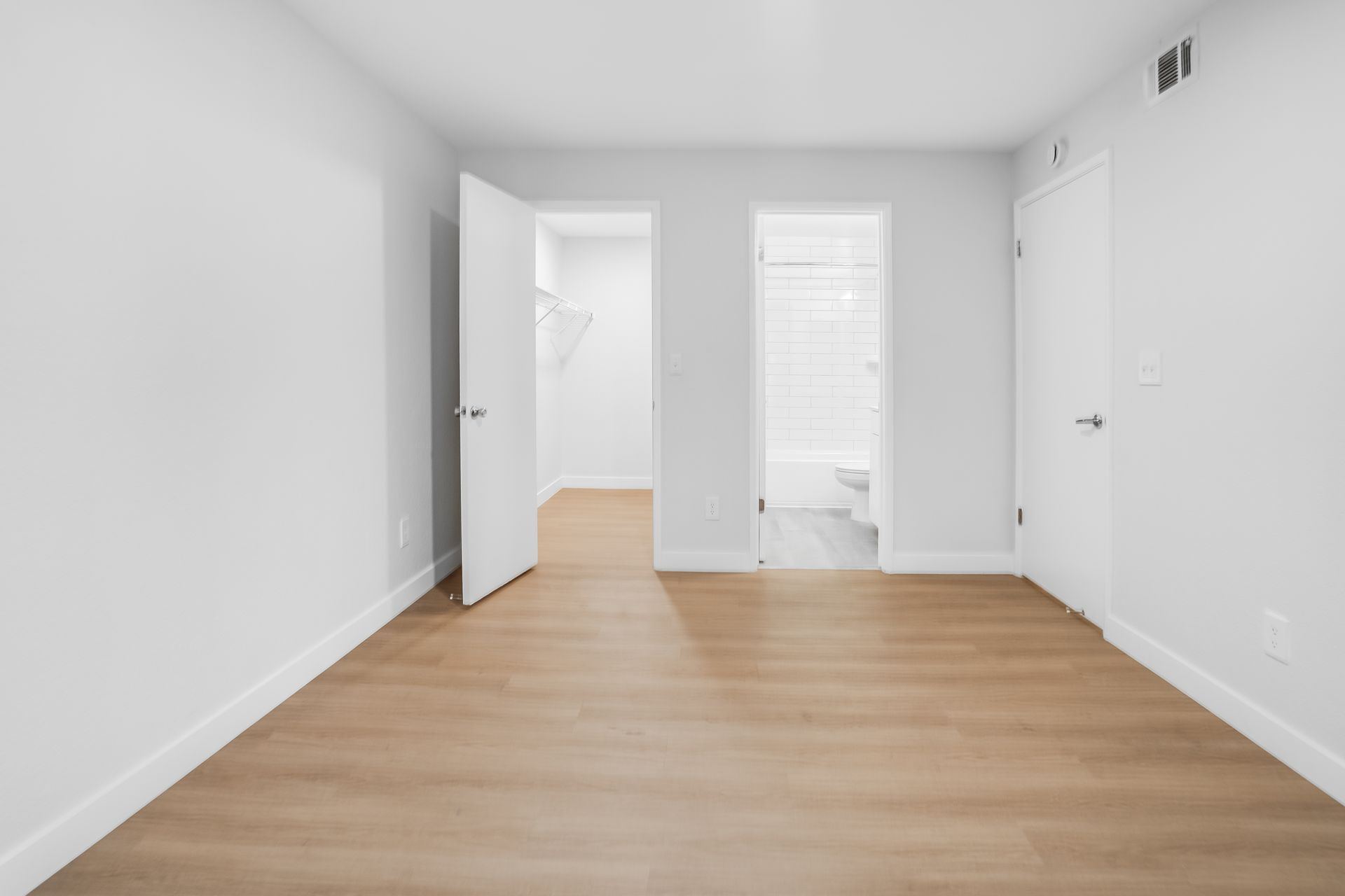 Empty bedroom with three doorways, wood floor, white walls.