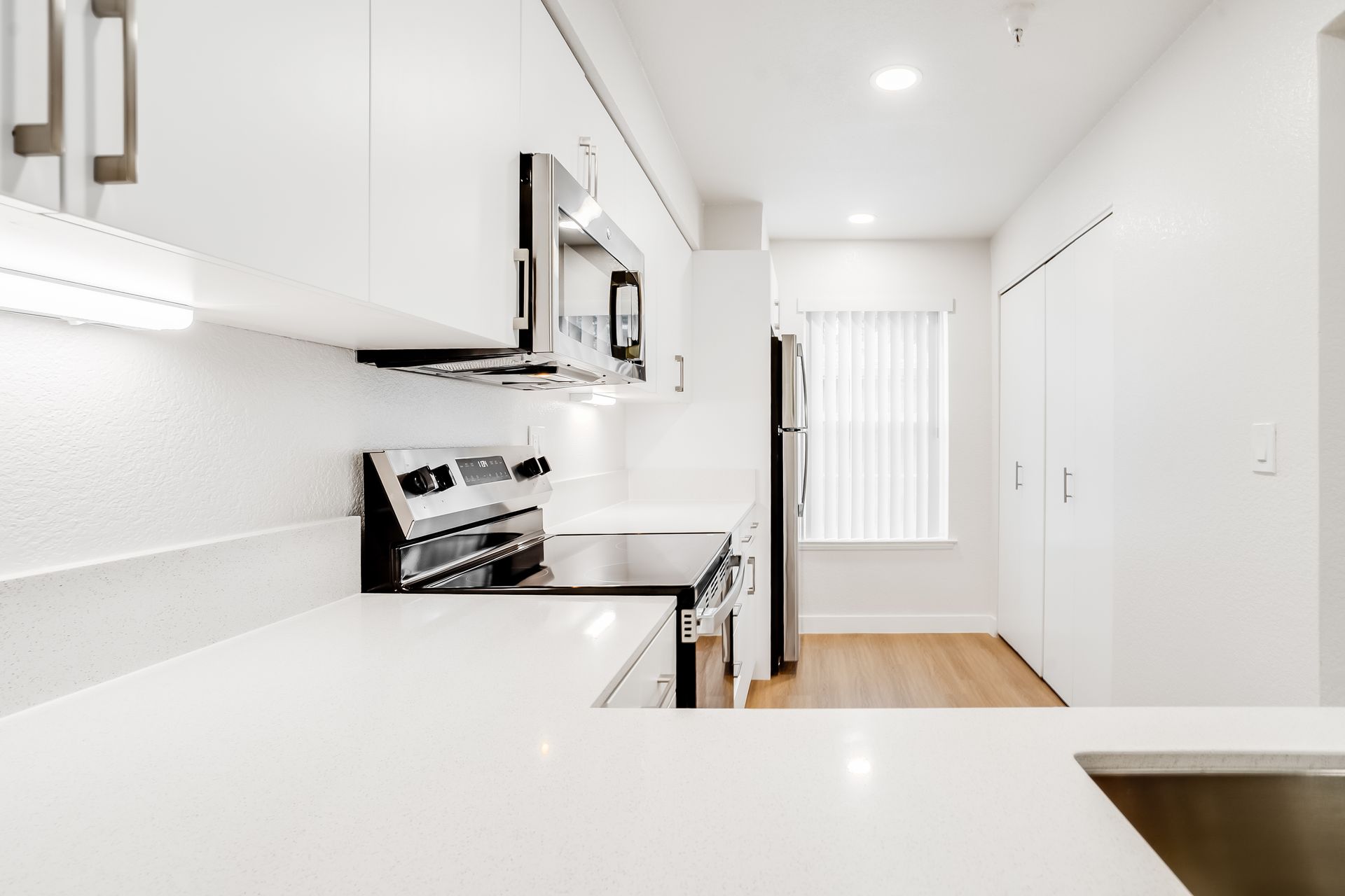 White kitchen with stainless steel appliances, countertops, and wood flooring.