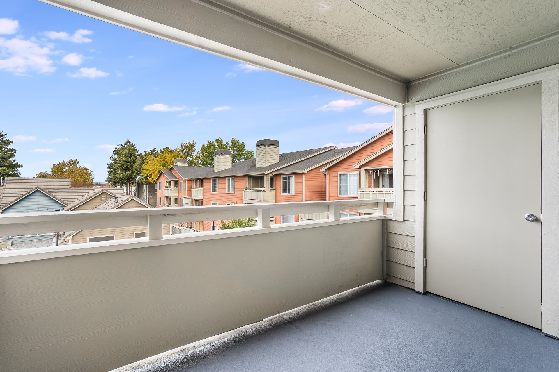 Balcony overlooking neighborhood with blue floor, white railing, and white door.