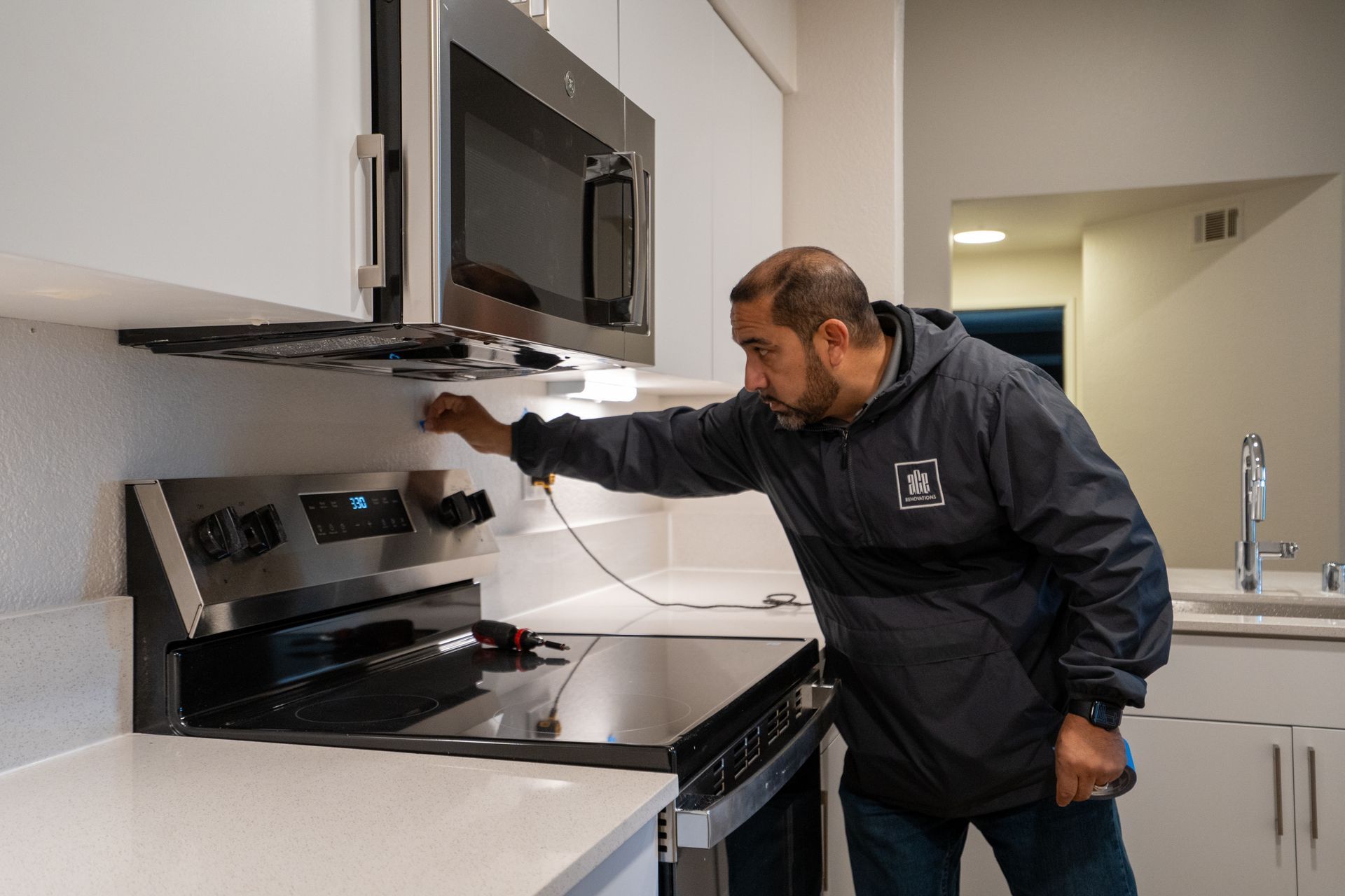 Man in a kitchen inspecting a stove. 