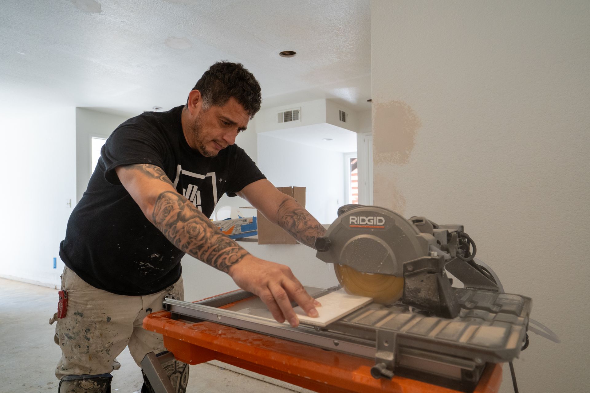 Man using a tile saw to cut a tile in a room under construction.