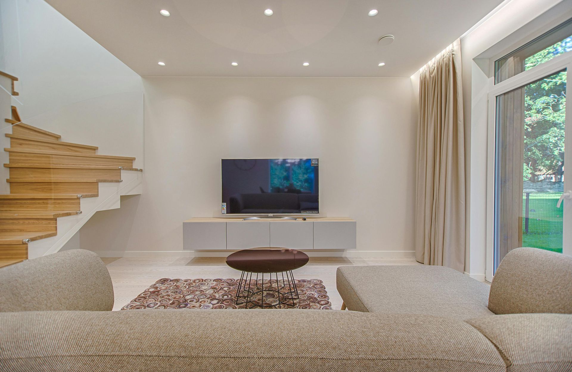 Living room with stairs, TV, sofa, and glass door leading outside.