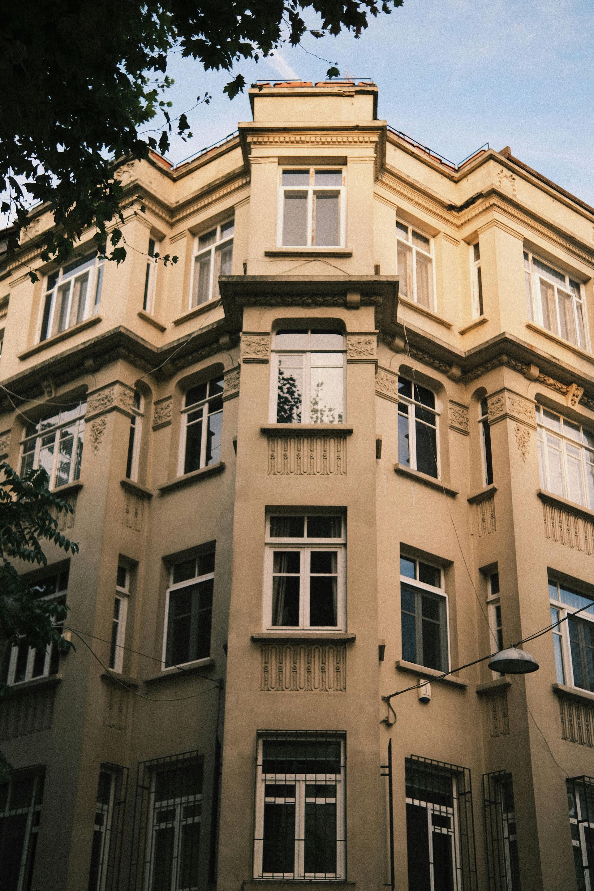 Tan corner building with multiple windows; tree branches frame the upper left.