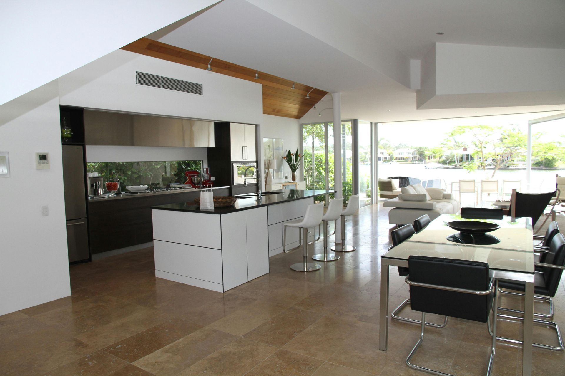 Modern open-plan kitchen and dining area with water view, white and gray with wood accents.