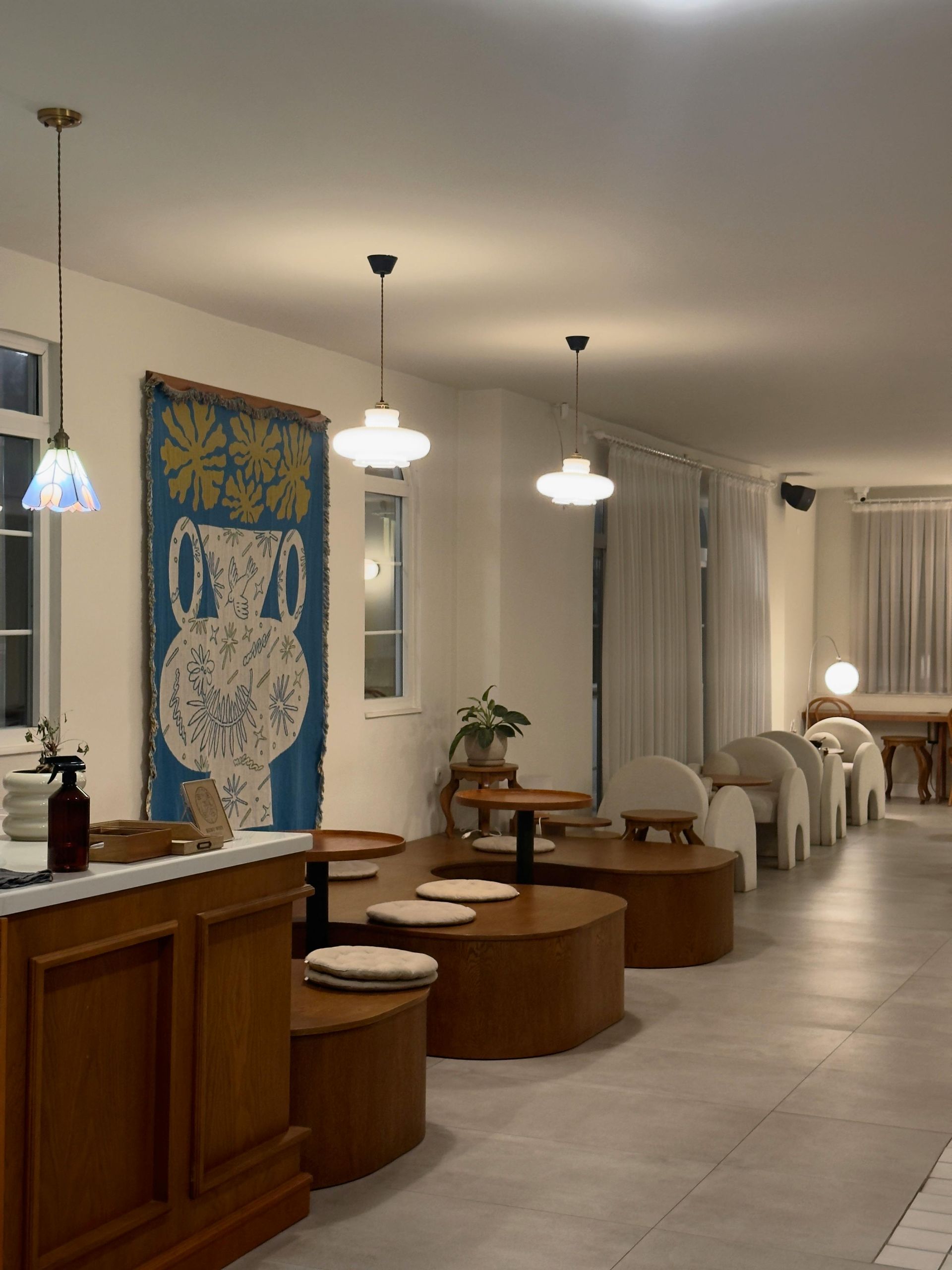 Cozy cafe interior with wooden tables, white chairs, blue rug, and hanging pendant lights.