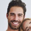 Smiling couple posing closely against a light background