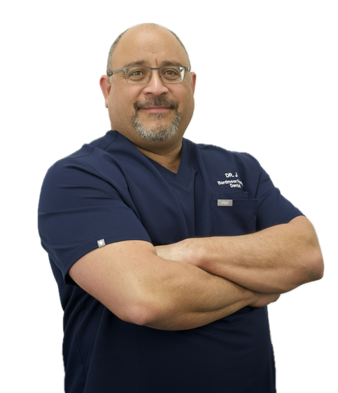 Smiling man in navy scrubs with arms crossed, standing against a white background