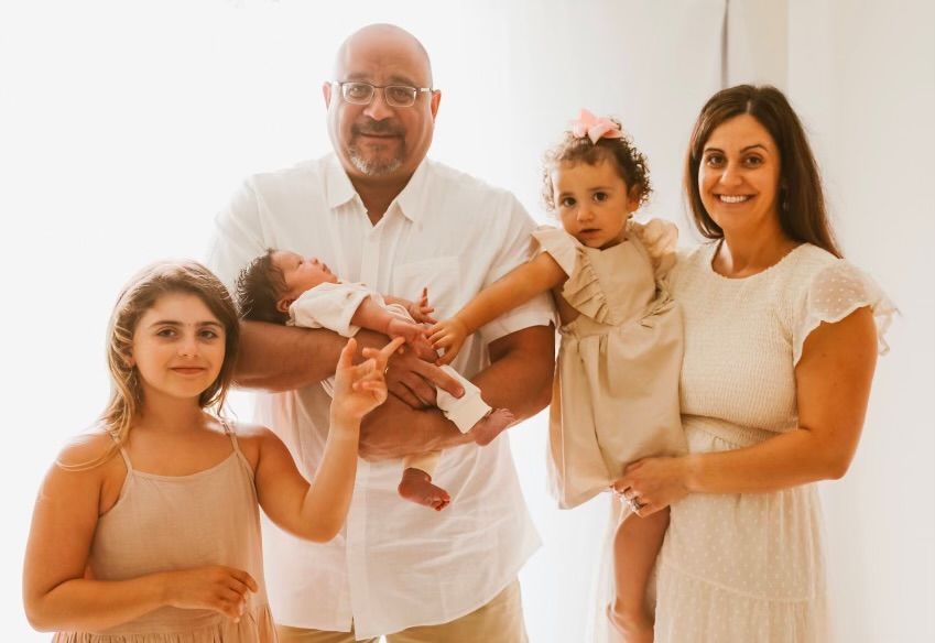 Family of four smiling and holding hands in a bright white room