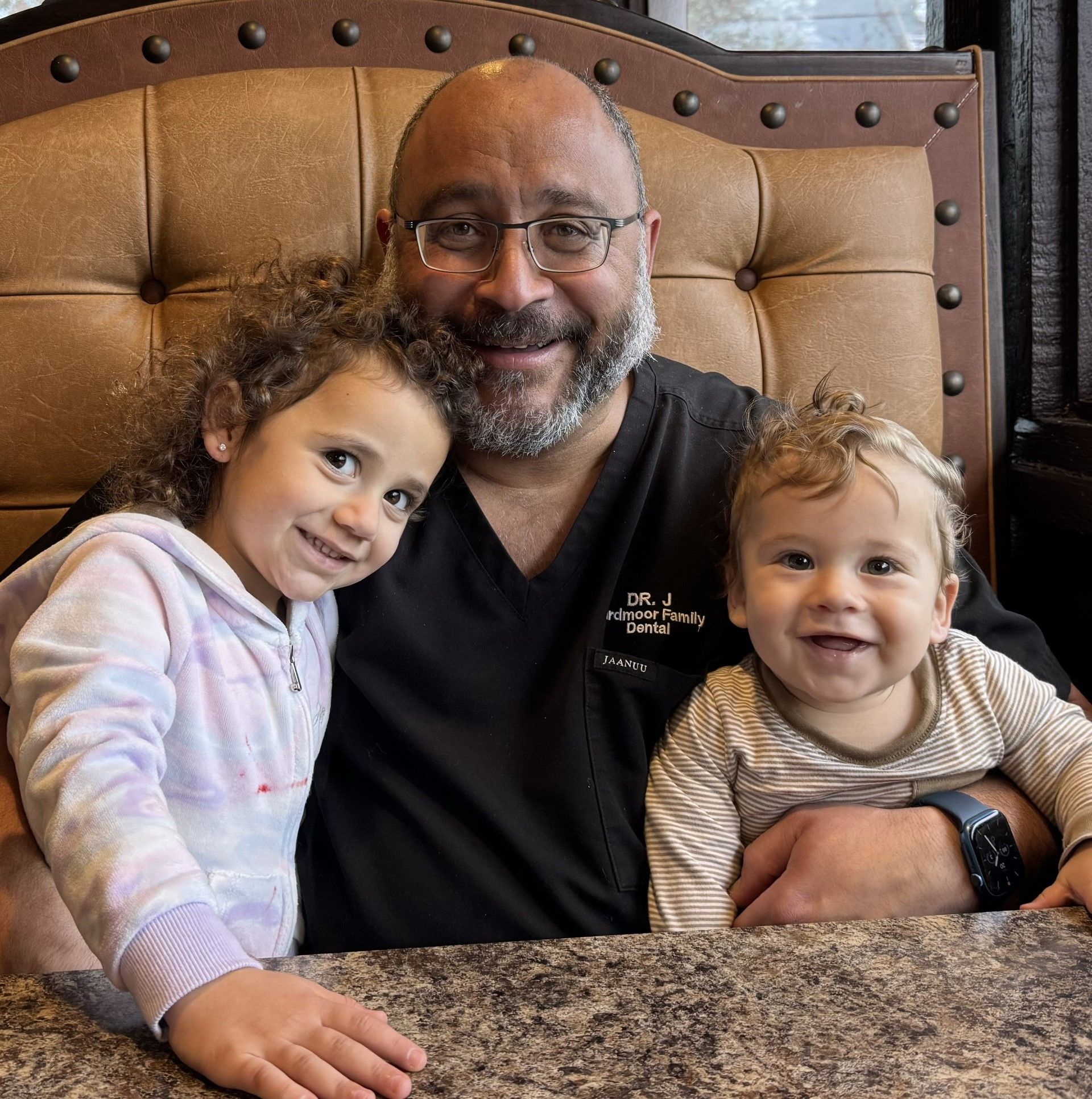 Smiling man with two children at a restaurant table, seated in a cushioned booth.