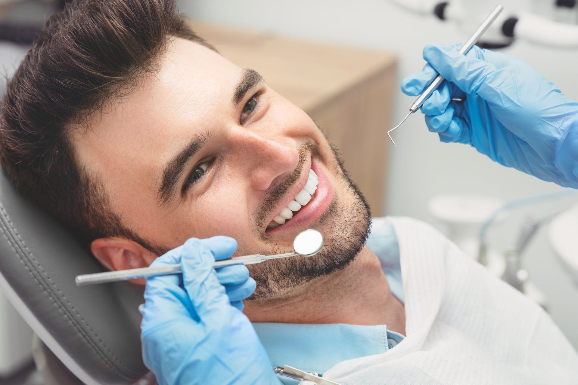 Dentist examining a smiling patient with a dental mirror and tools in a clinic