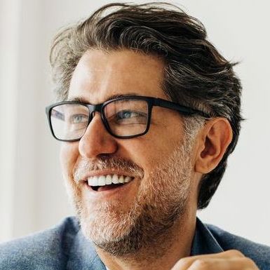 Smiling man with glasses in a blue shirt, looking off to the side