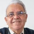 Smiling man with gray hair and glasses in a dark jacket, against a light background