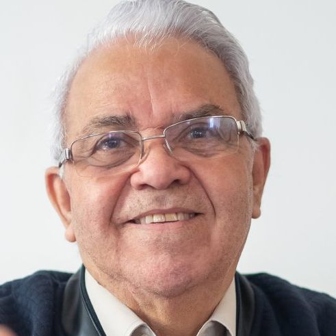 Smiling man with gray hair and glasses in a dark jacket, against a light background