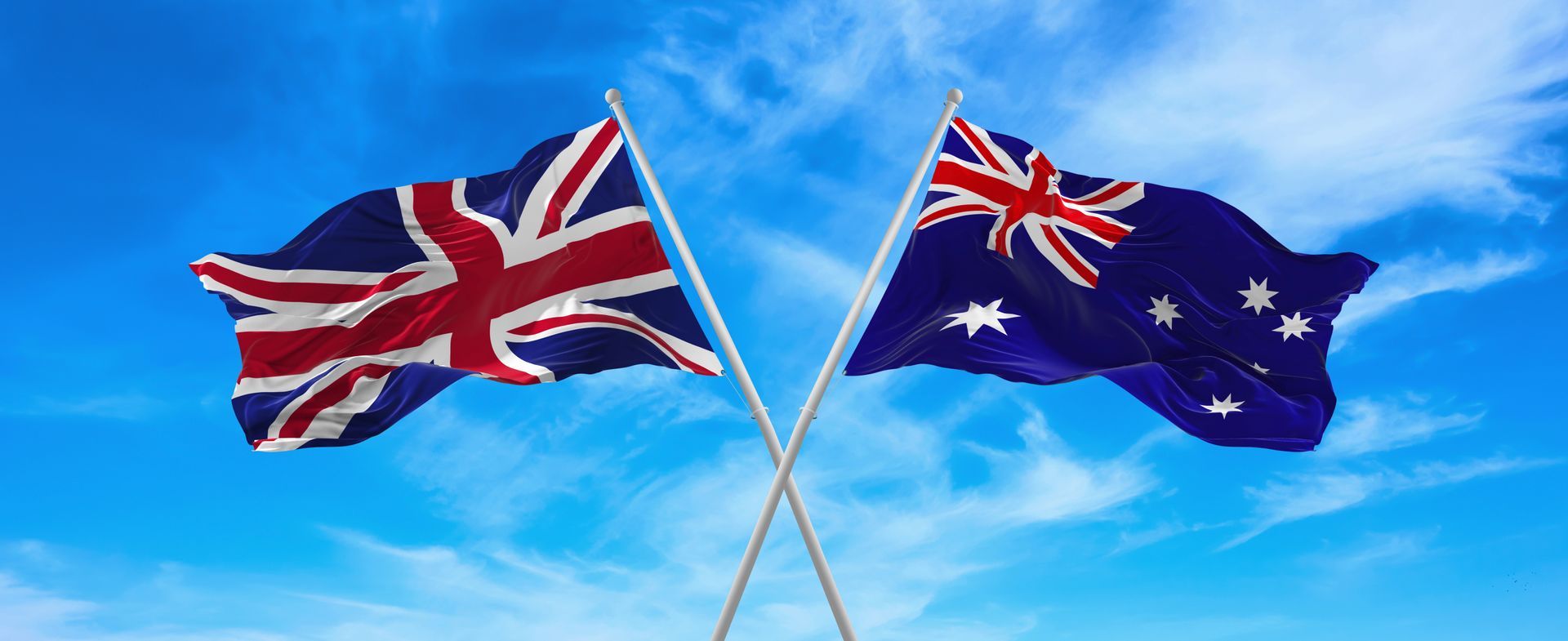 Two flags, the Union Jack and the Australian flag, crossed against a blue sky.