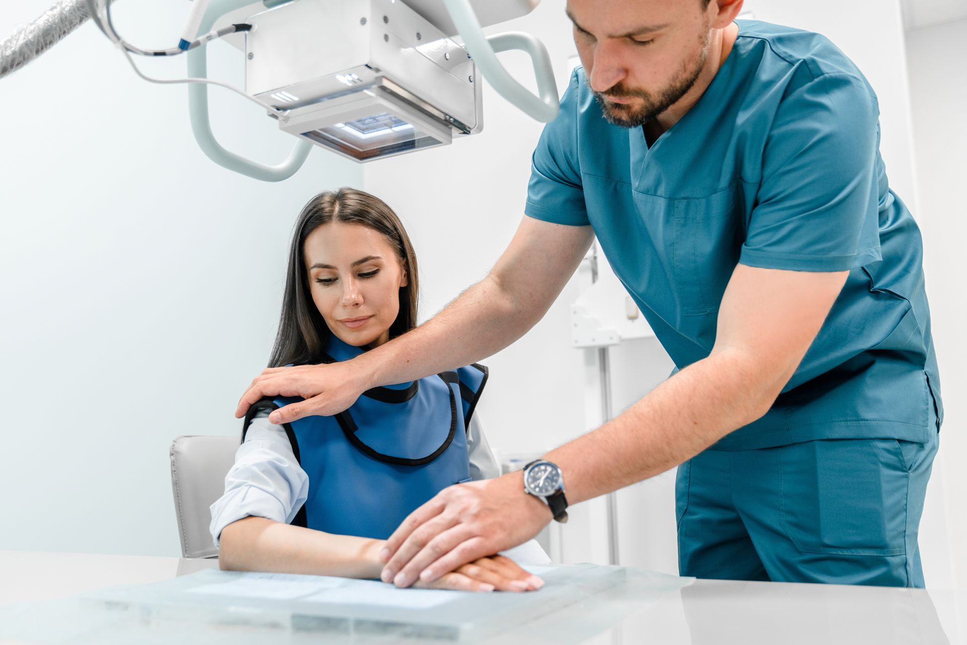 Radiographer leaning over a seated patient in a bright clinic room
