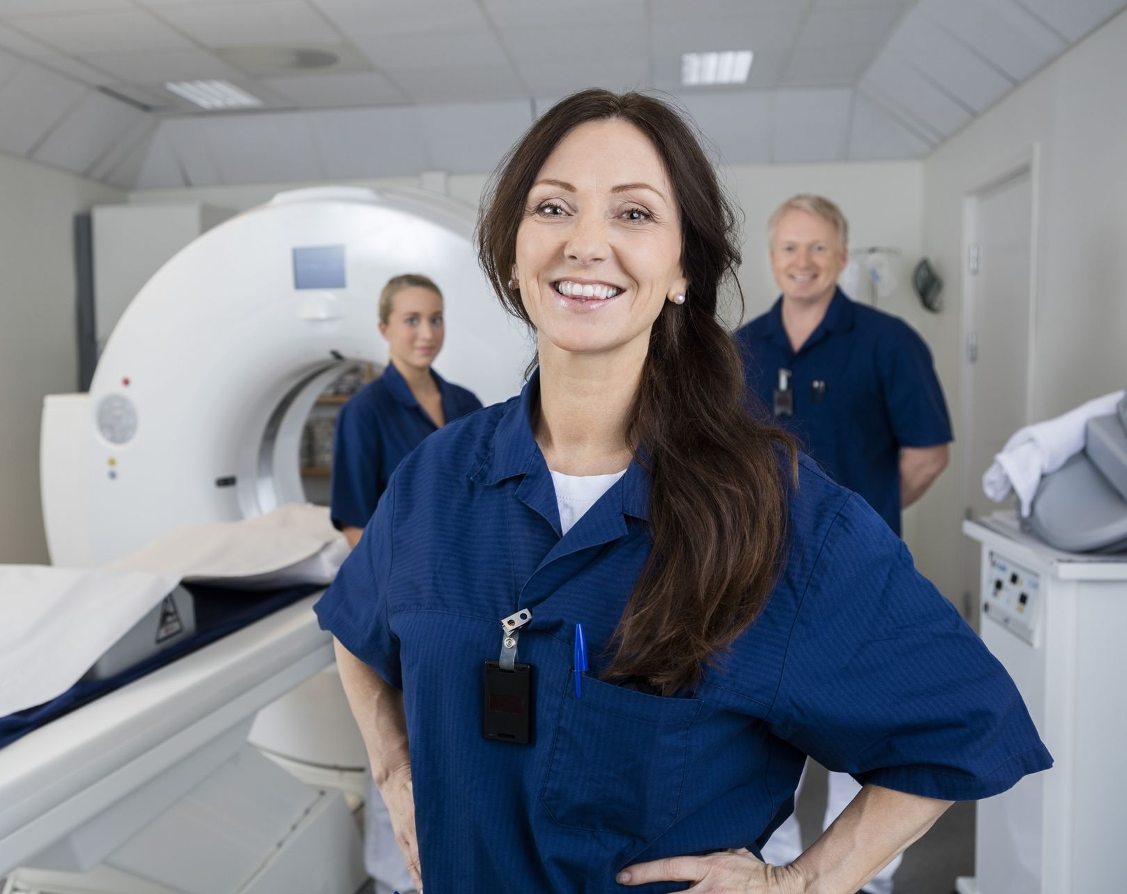 Radiology staff standing beside an MRI scanner in a bright clinic, with one woman smiling in the foreground