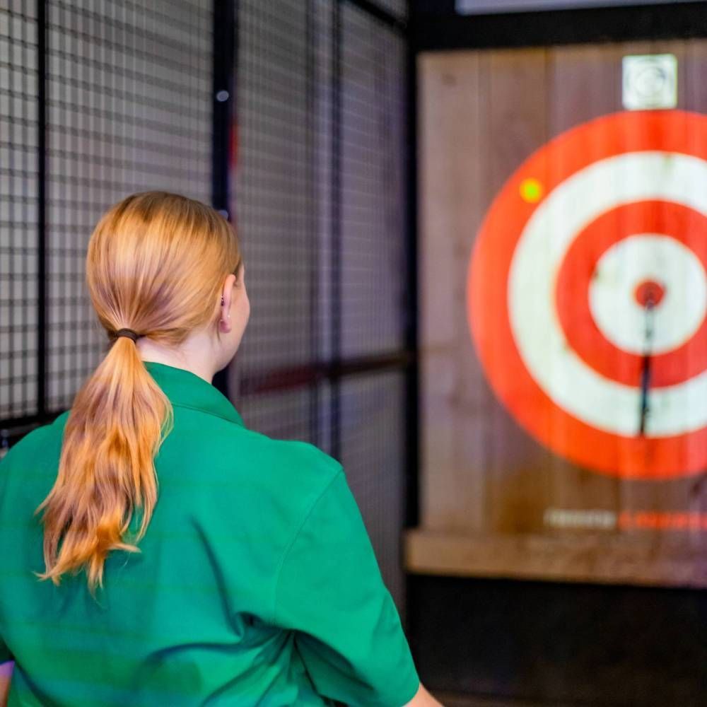 Person in a green jacket facing a red-and-white target in an indoor axe-throwing lane