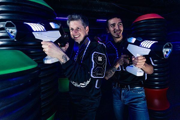 Two people in glowing laser tag vests aiming laser tag guns in a neon-lit arena