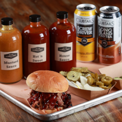 BBQ sandwich with sauces and pickles on trays, with four bottled sauces in the background